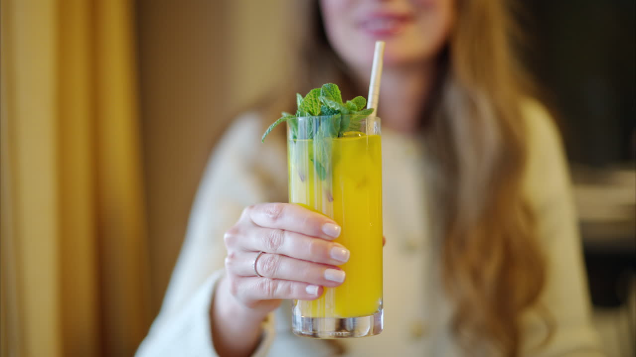Woman drinking fresh orange lemonade with mint leaves and paper straw