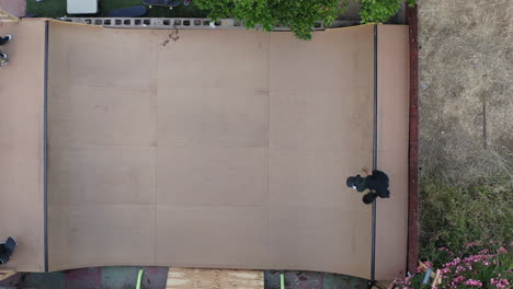 Skateboarder-dropping-into-mini-ramp-in-backyard-garden,-top-down-aerial-view