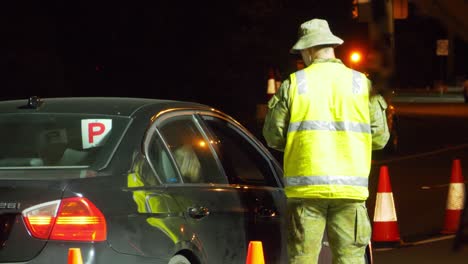 traffic guard in reflectorized jacket talking to a driver in black car at night - police checkpoint at gold coast, qld border - coronavirus pandemic restrictions in nsw, australia.  - medium shot
