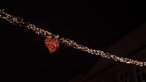 christmas and new year decorations of lights in a heart strung across main street in a town - night