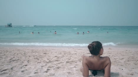 brunette in black bikini with open shoulders lies on beach