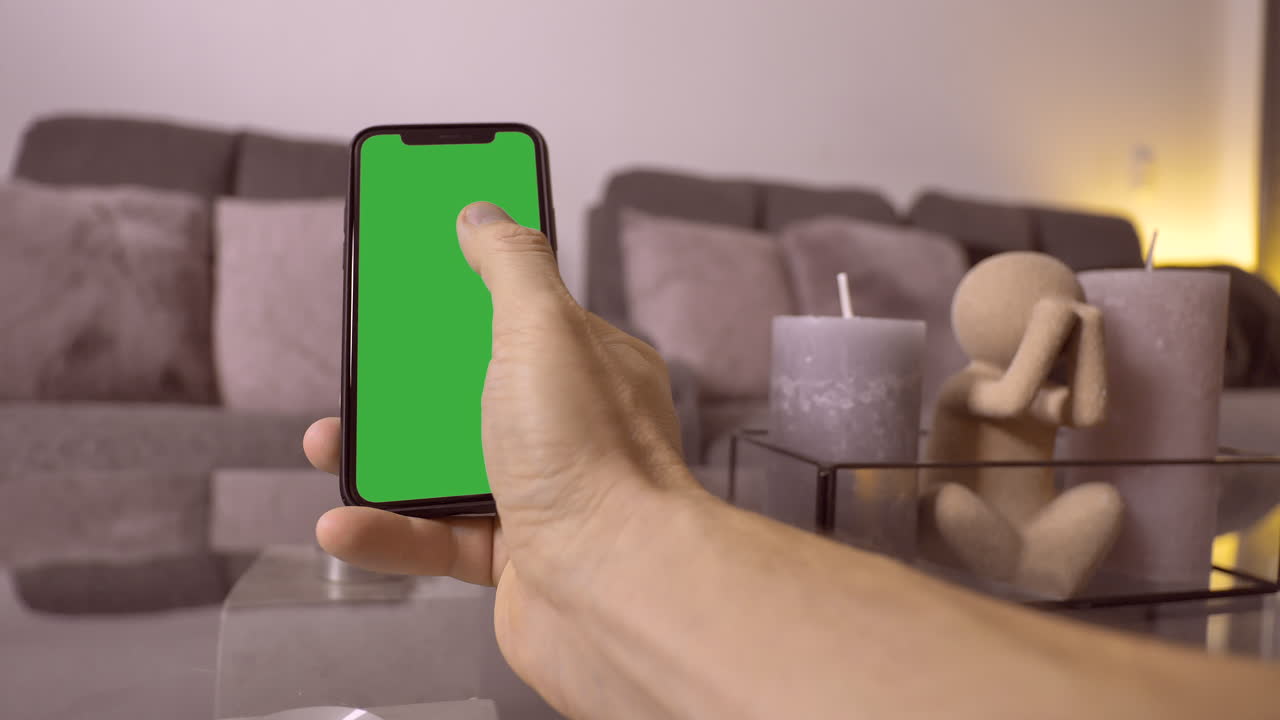 una persona del sexo masculino desliza la pantalla verde del teléfono móvil en casa en la sala de estar, de cerca - resolución prores 4k