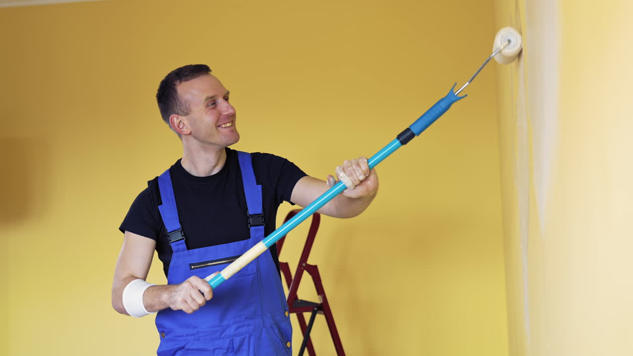 Young man painting wall with roller brush while renovating his apartment. Repair, building and home concept.