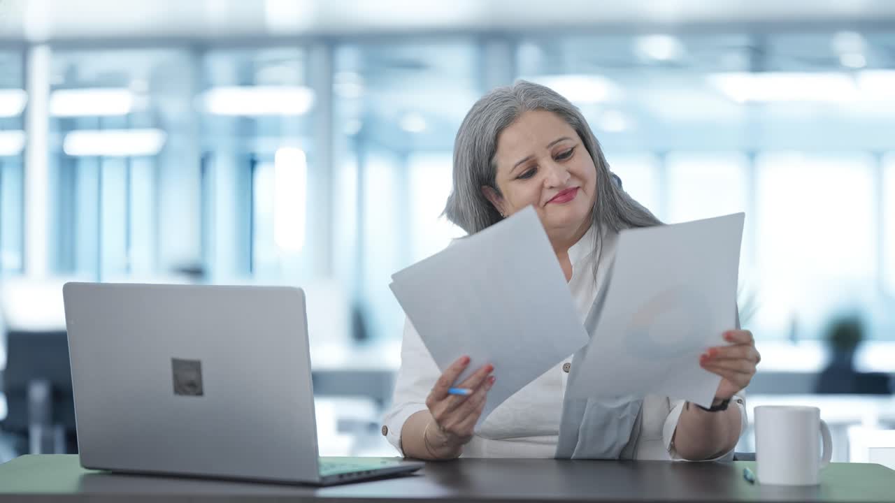 una mujer india alegre, gerente sénior, leyendo informes de negocios.