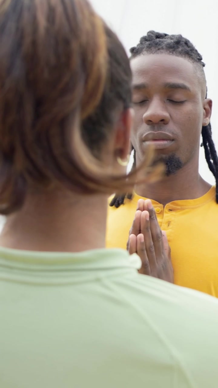 Vídeo vertical: Mulher com elástico de cabelo filmando em uma colina, homem entrando e juntando as palmas das mãos para meditar.