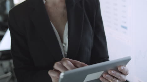 grey-haired businesswoman in glasses holding tablet and typing