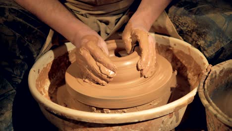 potters hands make a wide low bowl on a wheel.