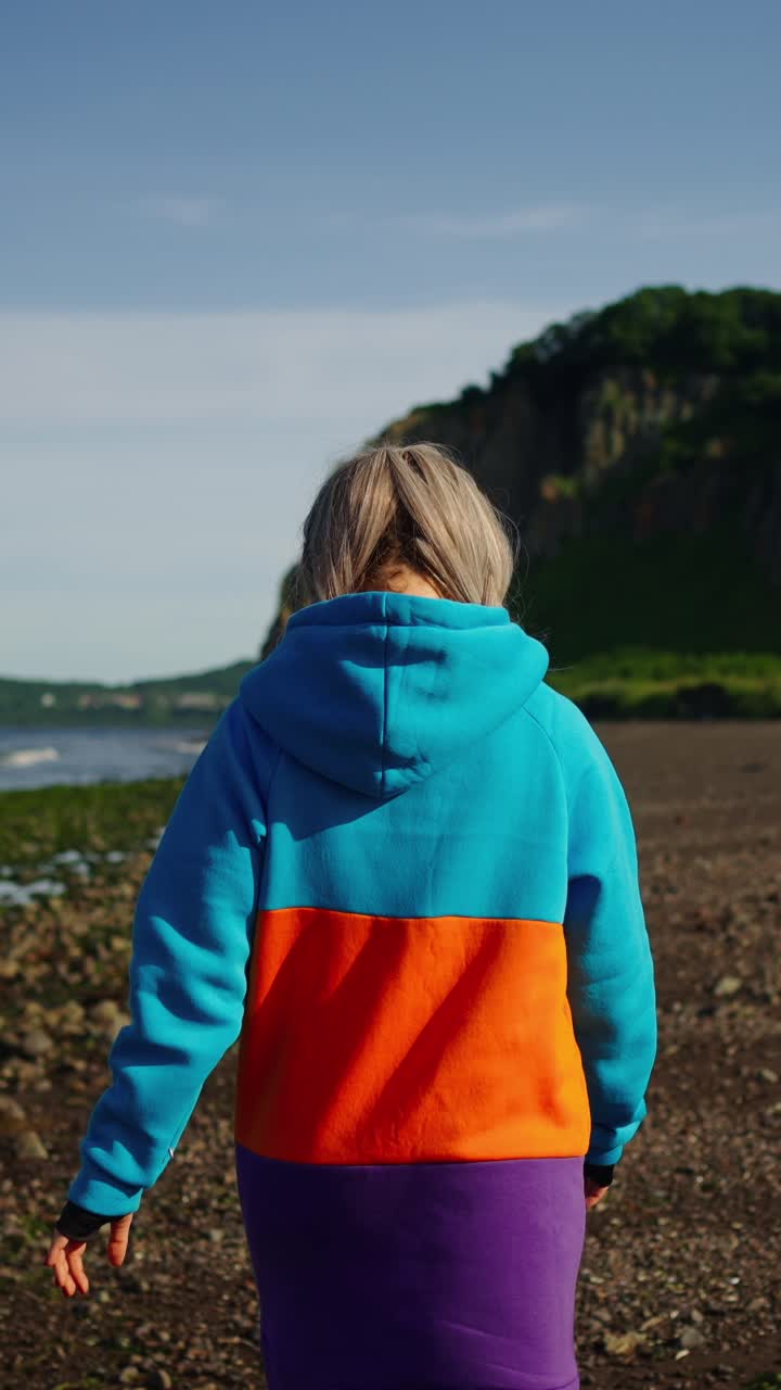 Jonge vrouw wandelt op rotsachtig strand richting de oceaan