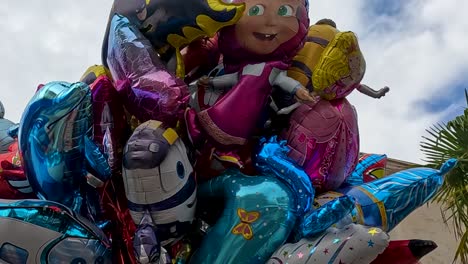 a cluster of colorful cartoon balloons floats beneath palm trees against a partly cloudy sky.