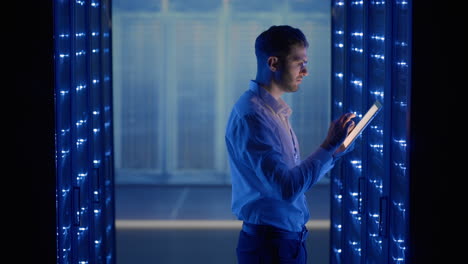 it technician in data center digital server room controlling work of rack server cabinets with a tablet. professional server engineer at work.