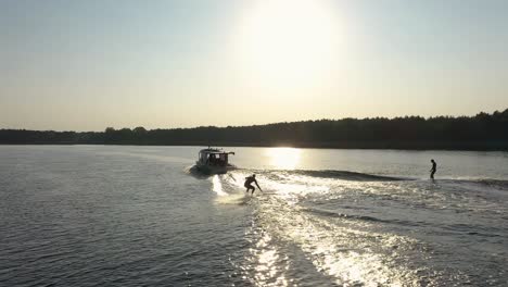 Two-surfers-on-surfboard-surfing-waves-behind-boat-in-sunset-004