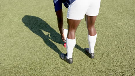 tying shoelaces, soccer african american male player preparing for game on grass field, copy space