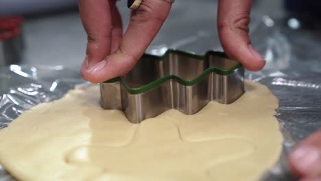 a hand pressing down a christmas tree shaped cookie cutter onto a circle of dough to create a tree shaped holiday christmas sugar cookie on a cold winter night