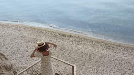 Mujer-Alegre-Girando-Sosteniendo-Sombrero-De-Paja-En-La-Escalera-De-Madera-A-Orillas-Del-Mar-Día-Soleado.