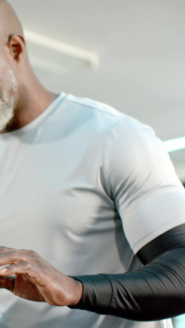 Video verticale: Uomo che afferra un manubrio, si prepara a sollevare pesi in palestra, indossando una manica a compressione.