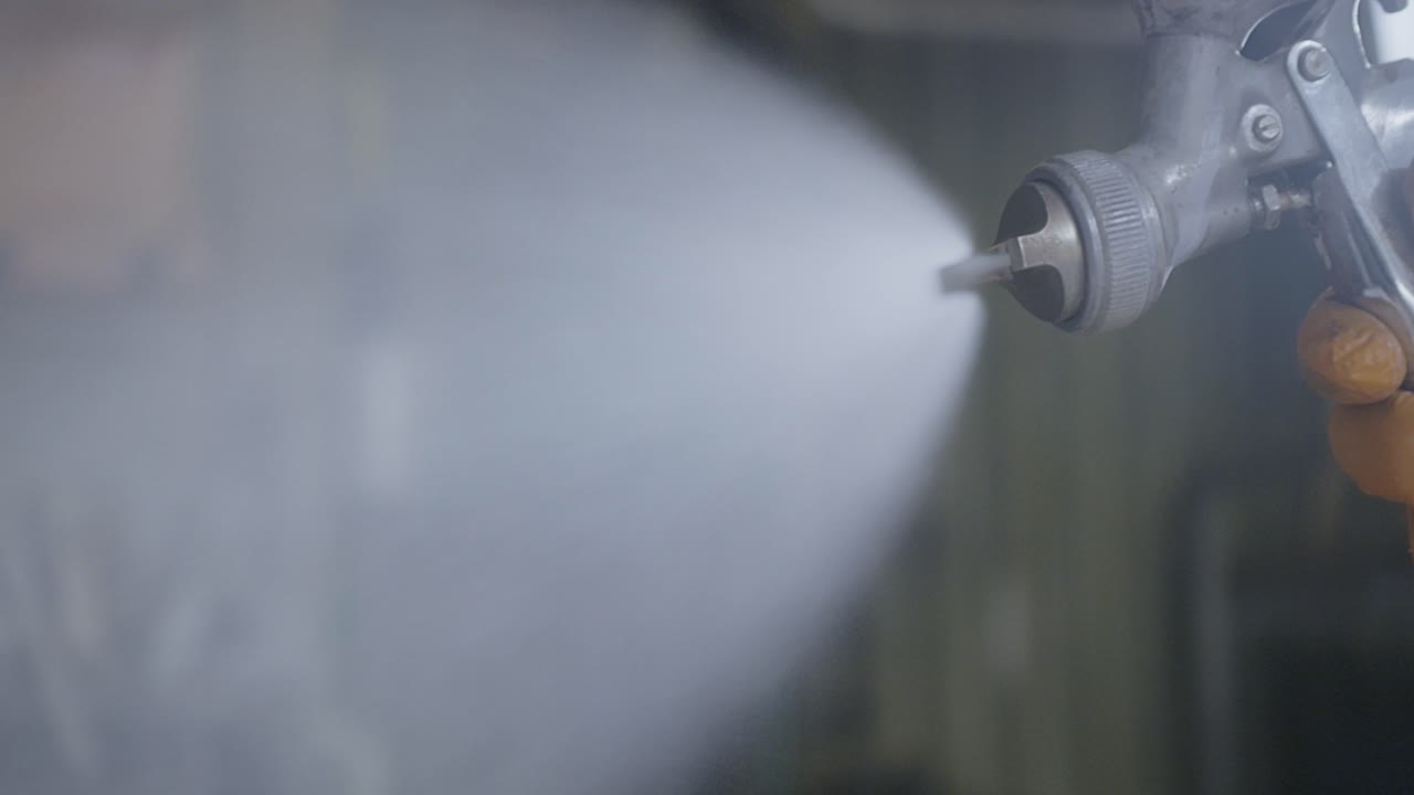 작업실에서 스프레이 권총을 들고 장갑을 입은 노동자