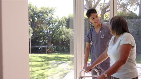 helping senior woman with walker, male physiotherapist smiling in bright room