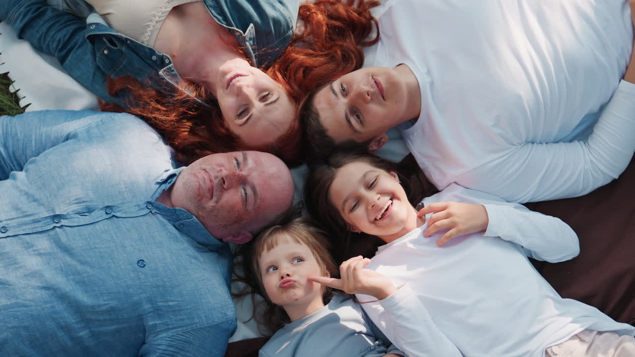 Aerial view of family discussing while lying faced up during picnic on blanket outdoors, sharing smiles and expressions of connection, warmth, love, and unity under natural sunlight