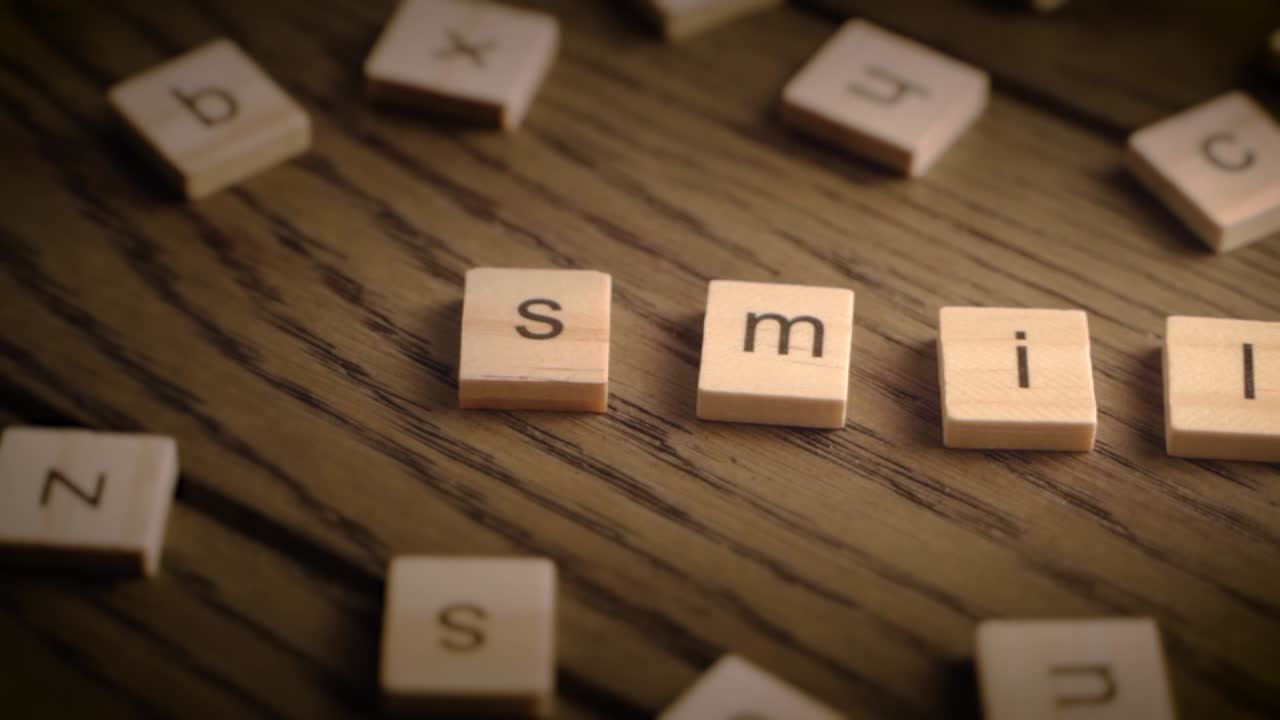 Wooden tiles spell the word smile as the camera pans smoothly across a rustic wooden surface in cozy lighting.