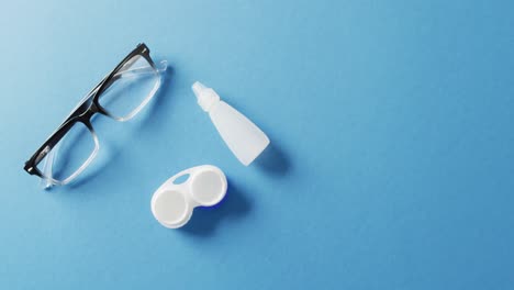 video of pair of glasses, contact lenses case and solution on blue background with copy space