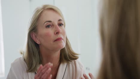 Caucasian-senior-woman-looking-in-bathroom-mirror-inspecting-her-face