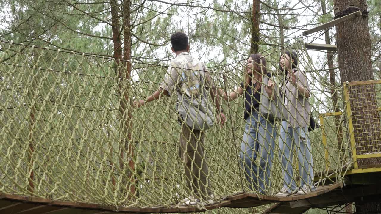 Young Asian Friends Crossing Rope Bridge in Forest Adventure
