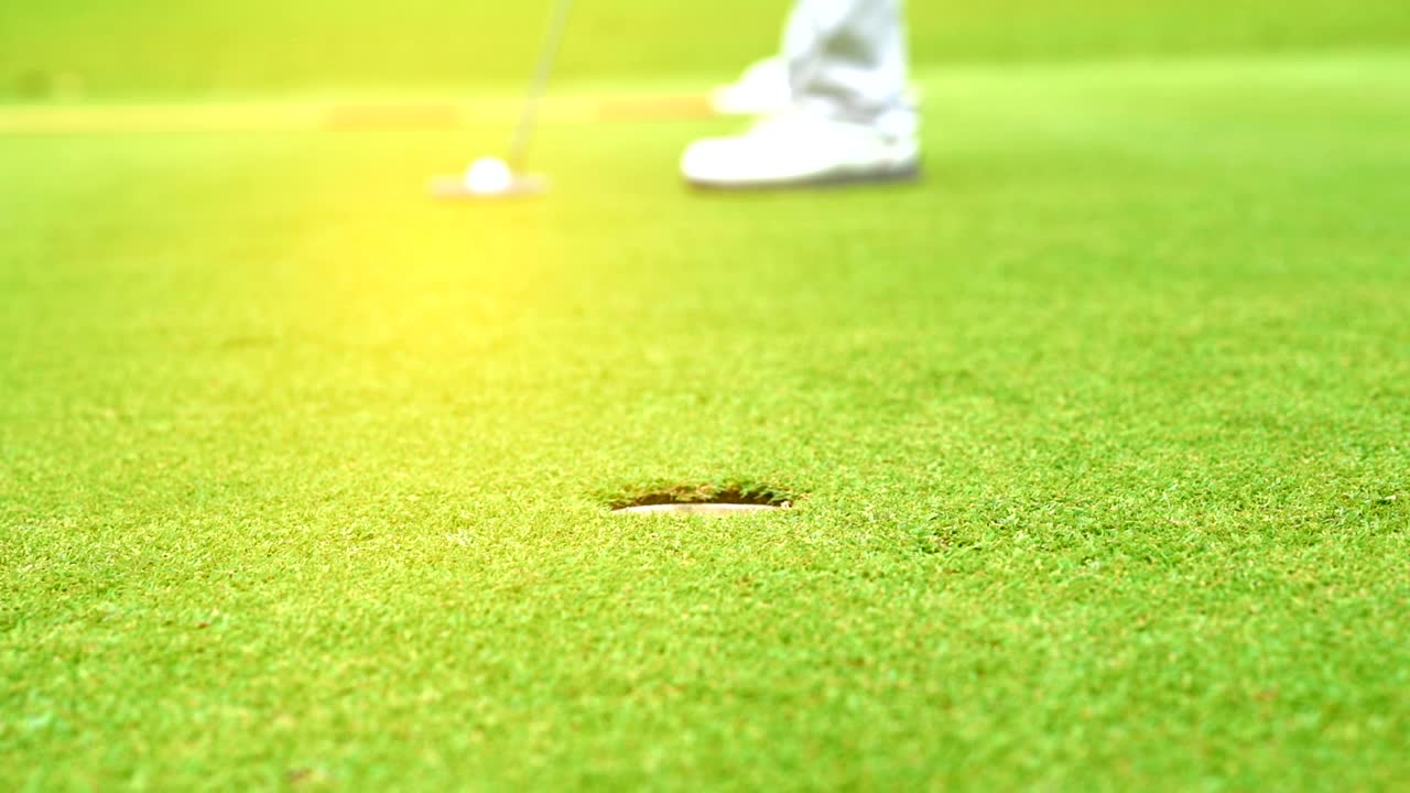 슬로 모션 골퍼가 골프 공을 구에 넣고 골프 코스에서 우승을 차지합니다. 해가 지는 아름다운 페어웨이입니다.