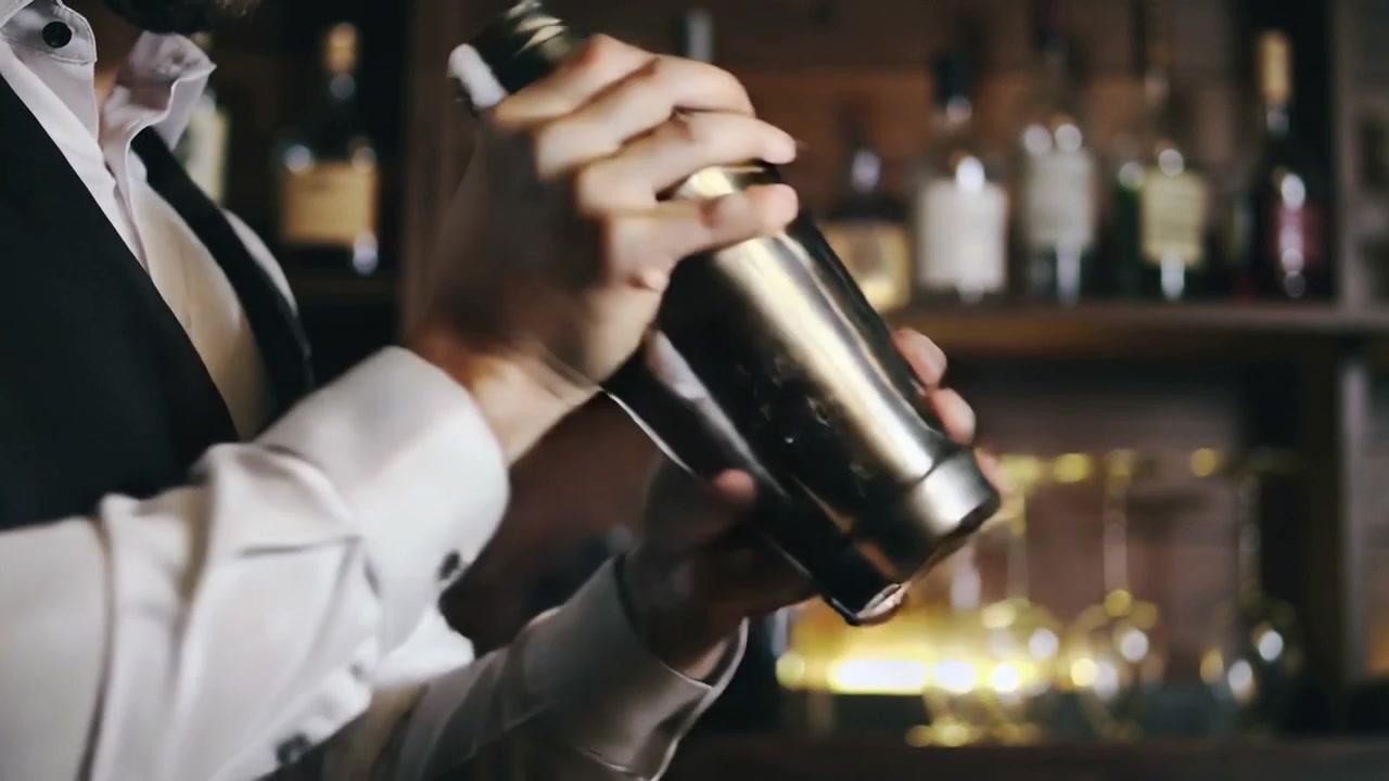 Barista che riceve un ordine, in camicia bianca e gilet scuro, che agita uno shaker al bancone preparando un drink, spazio per il testo.