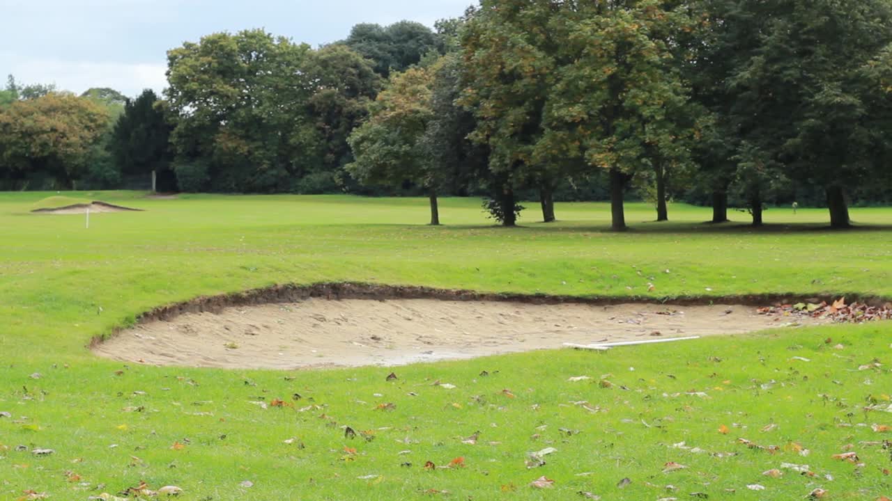A slow pan left to right of a golf hoel with a sand bunker and leaves on the ground.