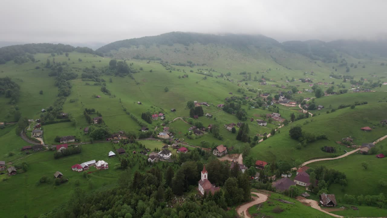 un pueblo de niebla con una iglesia en medio de colinas verdes, vista aérea