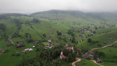 a foggy village with a church amidst green hills, aerial view