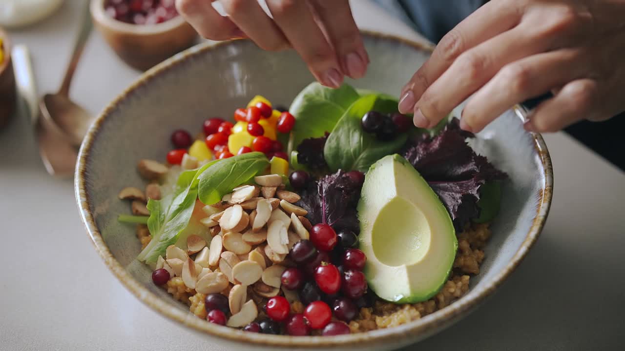 Close-up showing hands sprinkling almond slices, arranging greens on grains for plating in kitchen