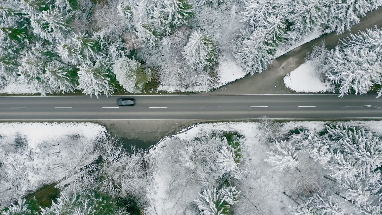directamente desde arriba - un coche de conducción rápida está acelerando a través de un paisaje de bosque invernal con tomas de arriba hacia abajo de árboles cubiertos de nieve al lado de una calle