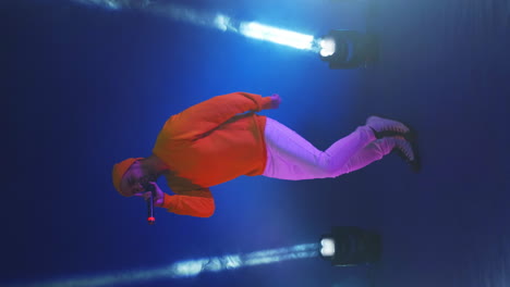 video vertical. un hombre con una chaqueta amarilla bailando sobre un fondo azul. cantante en el estudio con luz de neón bailando y cantando