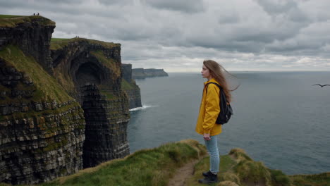 woman standing on a cliff overlooking the ocean at the cliffs of moher