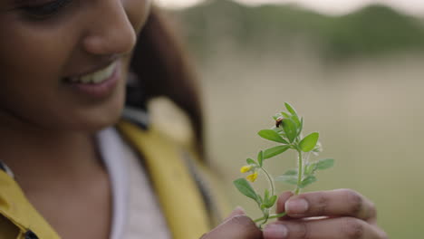 Primer-Plano-De-Un-Insecto-Mariquita-Arrastrándose-Sobre-Una-Hoja-Verde-Una-Joven-India-Sosteniendo-Una-Planta-Sonriendo-Disfrutando-Mirando-Una-Pequeña-Y-Colorida-Mariquita