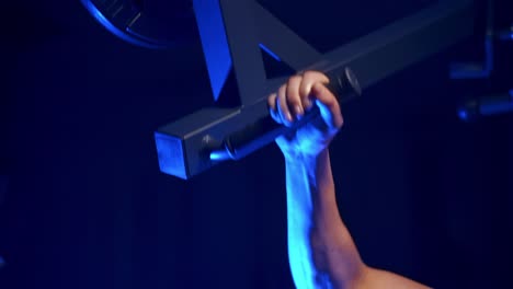 bodybuilder doing workout in the gym. strong man with naked torso training his muscles on a simulator. close-up. blue filter.