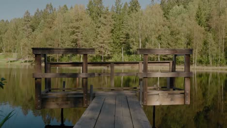 Puente-De-Madera-En-El-Lago-Kypesjön-En-Borås,-Suecia-A-Finales-De-La-Tarde-De-Verano---Toma-Amplia-Que-Avanza-Y-Gira-A-La-Izquierda