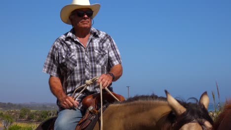 a senior cowboy rides his horse with large hat on a ranch