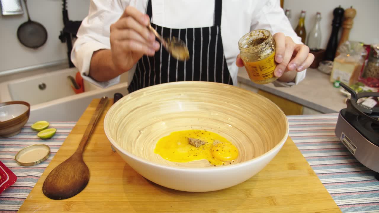 el chef agrega el ingrediente especiado en un recipiente hondo con ingredientes para la salsa de ensalada césar