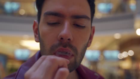 street magic artist in red leather jacket bites out - off a coin in half and blowing it back onto coin while smokes coming out of his mouth at public mall, close up shot