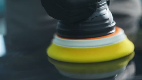 macro shot of yellow sponge head of polisher machine removing scratches from car hood