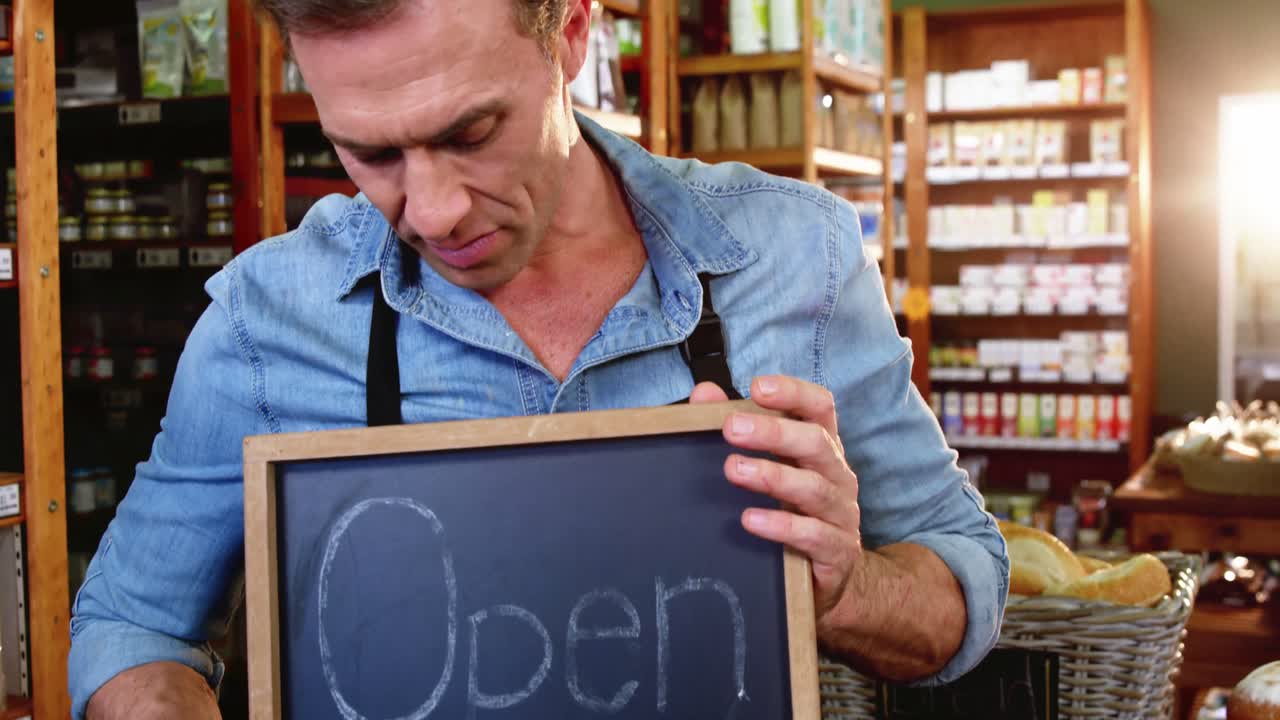 Männlicher Mitarbeiter hält ein Geöffnet-Schild im Supermarkt