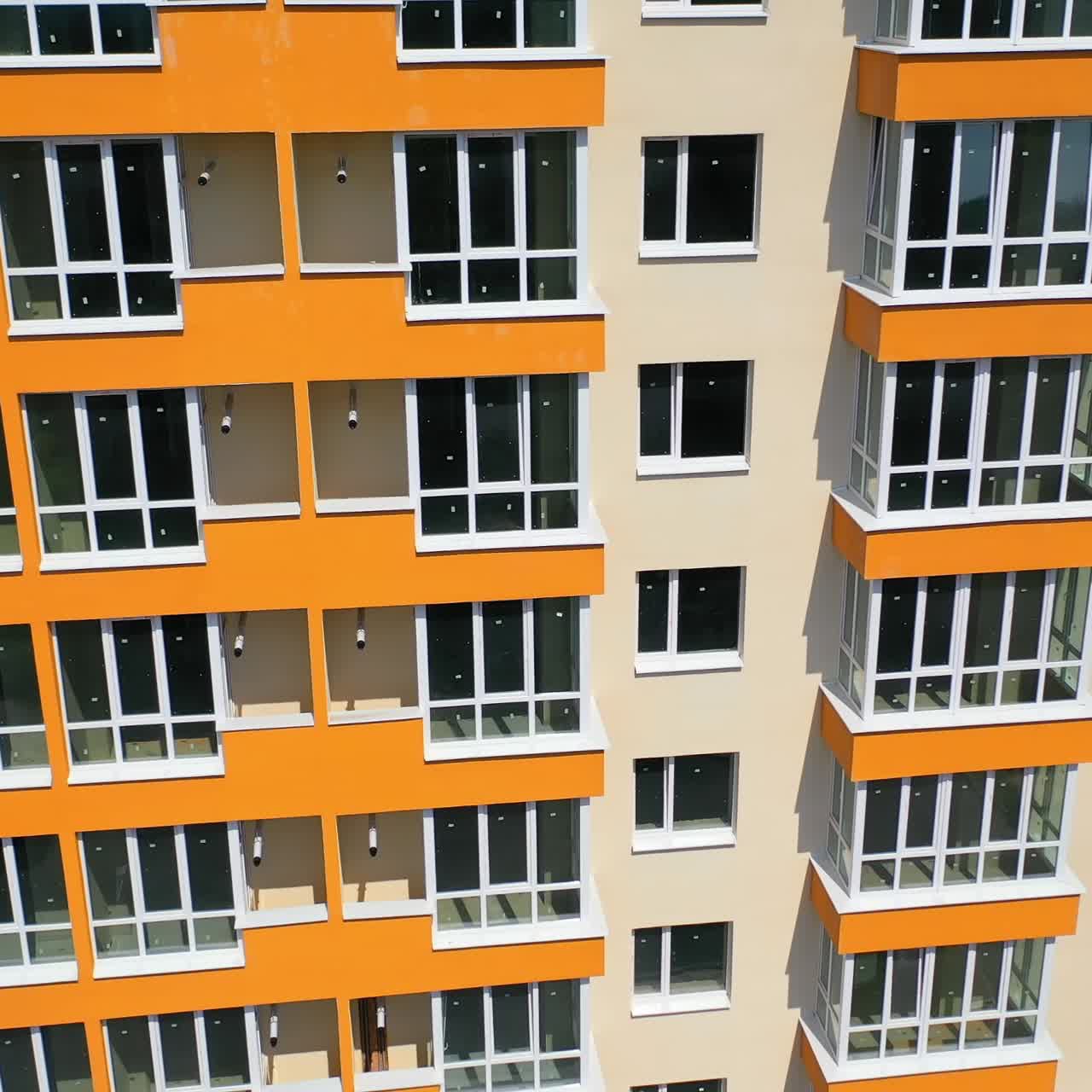 Building exterior of city multi-story apartment building. Facade of skyscraper building with new plastic windows and orange balconies at sunshine