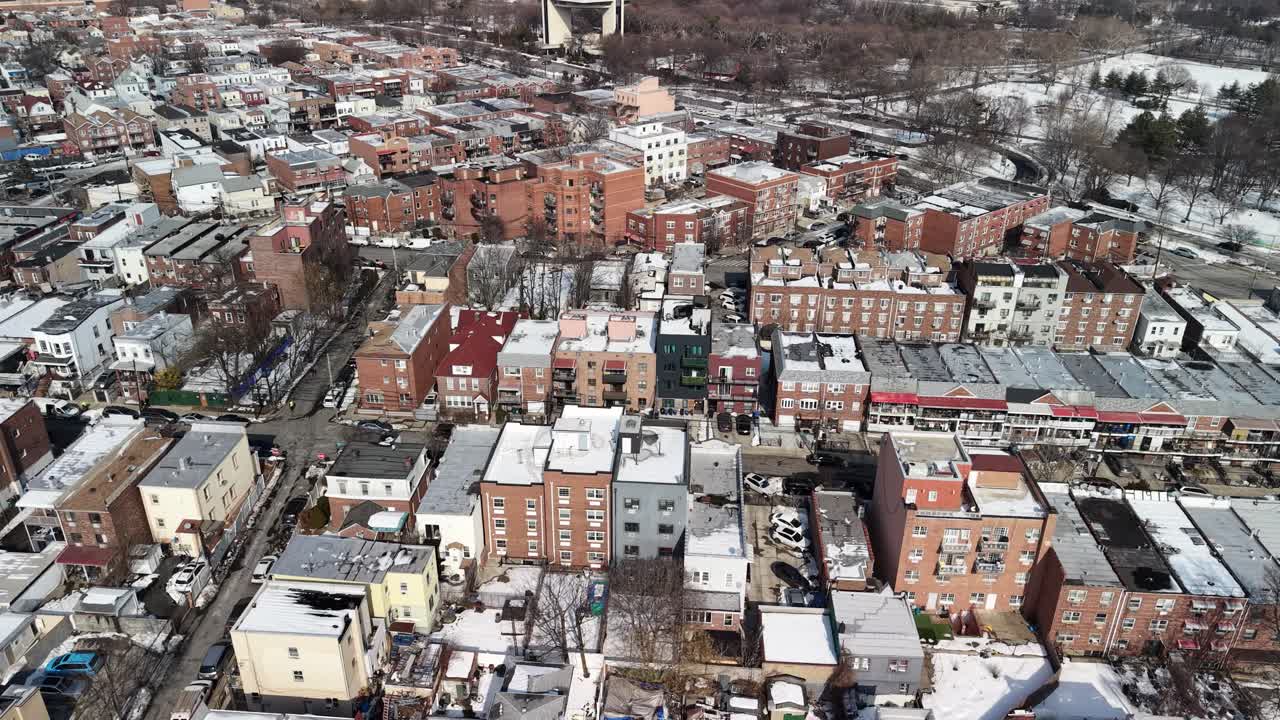 Urban landscape with residential buildings and snow covered rooftops during winter, showing a bird's eye perspective of the city streets and a nearby park on a sunny day