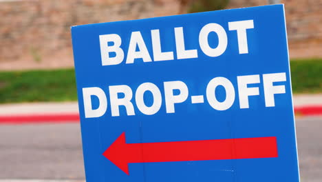 blue ellection ballot drop-off sign with red arrow pointing left and blowing in the wind outside