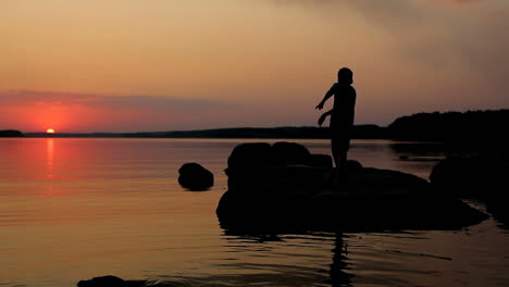 boy playing on stone. young child playing on stone near water at sunset