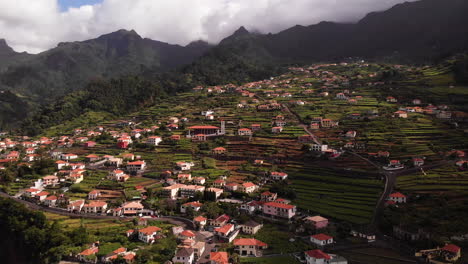 Vista-Aérea-De-Un-Pequeño-Pueblo-En-La-Cima-De-Una-Colina-Verde-Con-Casas-Adosadas-En-Un-Paisaje-Montañoso,-Sao-Vicente,-Madeira,-Tiro-De-Establecimiento