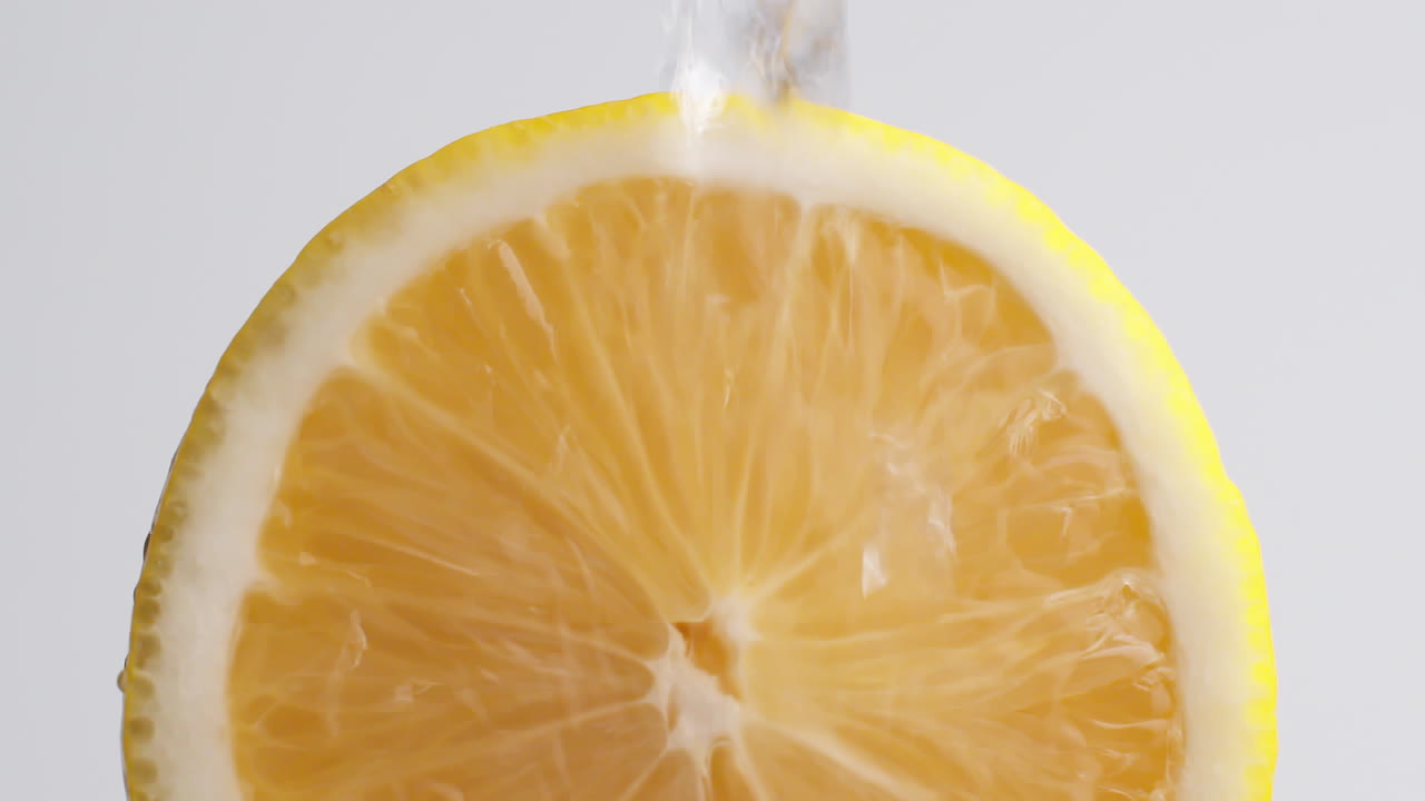 tiro macro de cámara lenta de agua que fluye de la rodaja de limón sobre fondo blanco