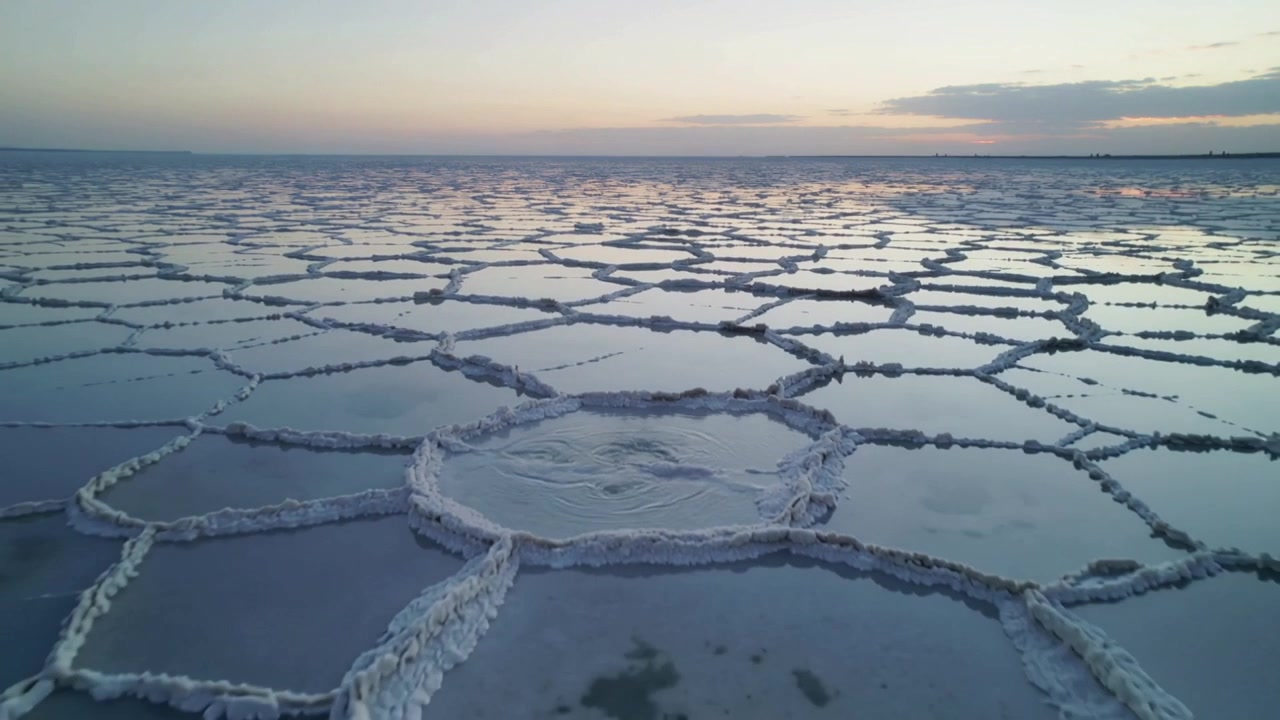 Gliding drone filming hexagon salt pans at sunset, splash creating circular ripples, reflecting sky